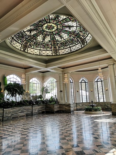 Elegant interior with a stained glass ceiling and patterned floor, featuring potted plants, located at Casa Loma in Toronto.