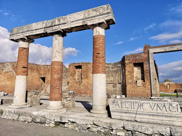 Ancient stone columns and ruins in Pompeii against a blue sky.