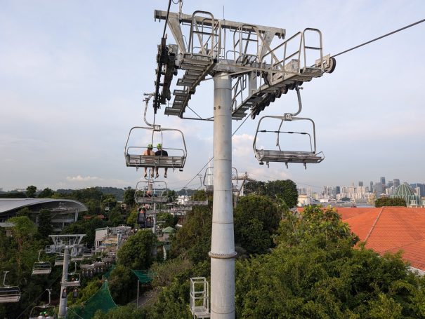 Aerial view of a cable car system in a green urban area with a skyline in the distance.