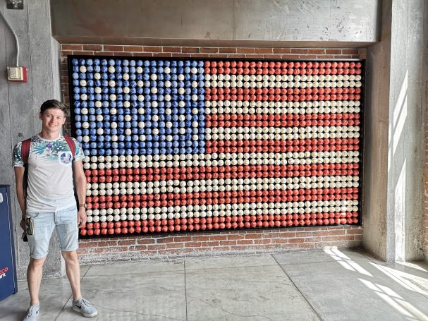 I&B's Founder's Husband posing in front of a USA flag made from coloured red, white and blue baseballs at Petco Park in San Diego