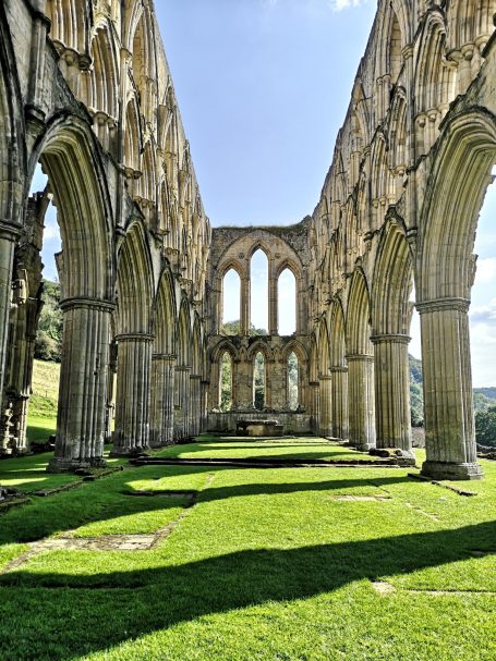Ruins of the grand stone structure known as Rievaulx Abbey with arches and lush grass underneath.