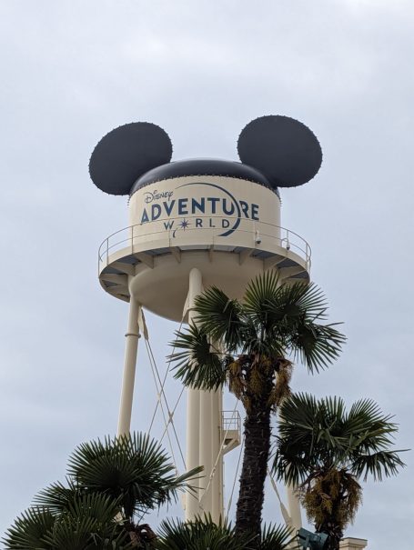 Water tower with Mickey Mouse ears, featuring "Adventure" signage, surrounded by palm trees.