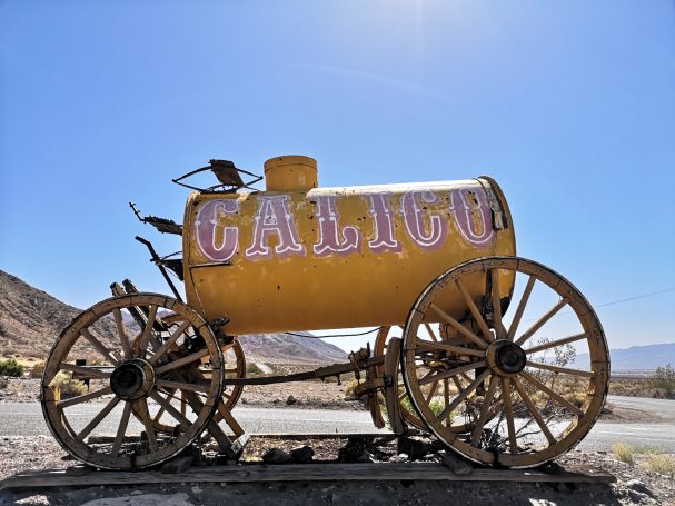Rusty yellow water wagon on wooden wheels, with "Calico" painted on the side, located at Calico Ghost Town in California.