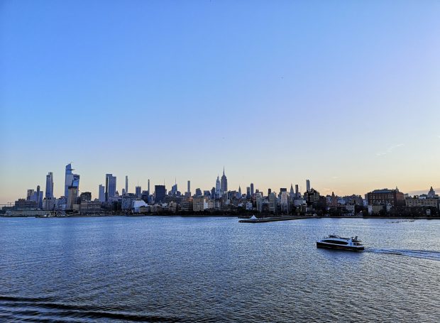New York City skyline view at sunrise, with a boat on a river in the foreground.