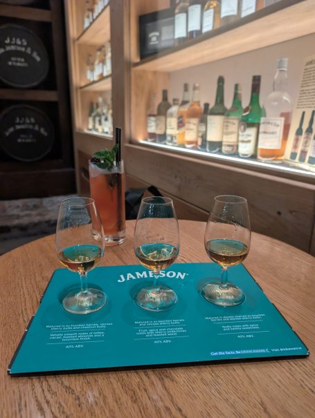 Glasses of whiskey on a tasting menu, with a cocktail in the background.