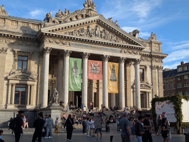 Historic building with grand entrance, columns, and banners, surrounded by people.