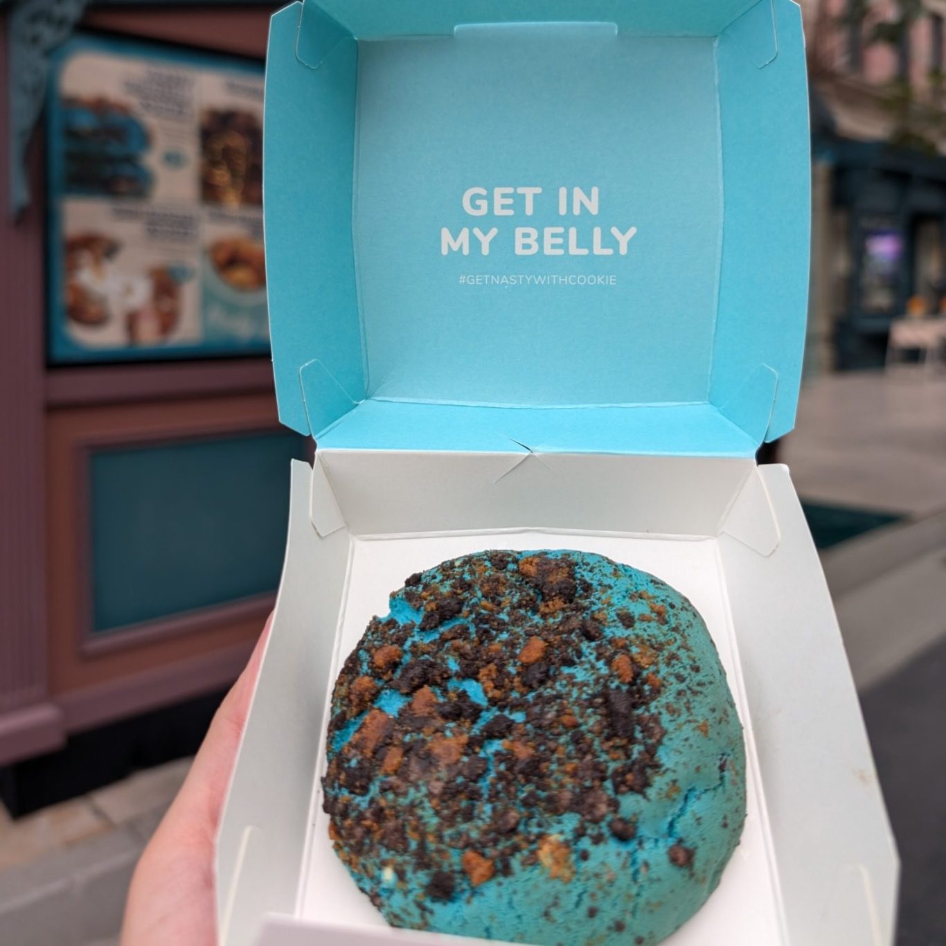 A blue cookie with chocolate chunks in a takeaway box.