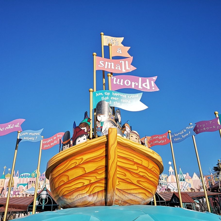 Colourful boat with flags, part of a theme park attraction, under a clear blue sky.