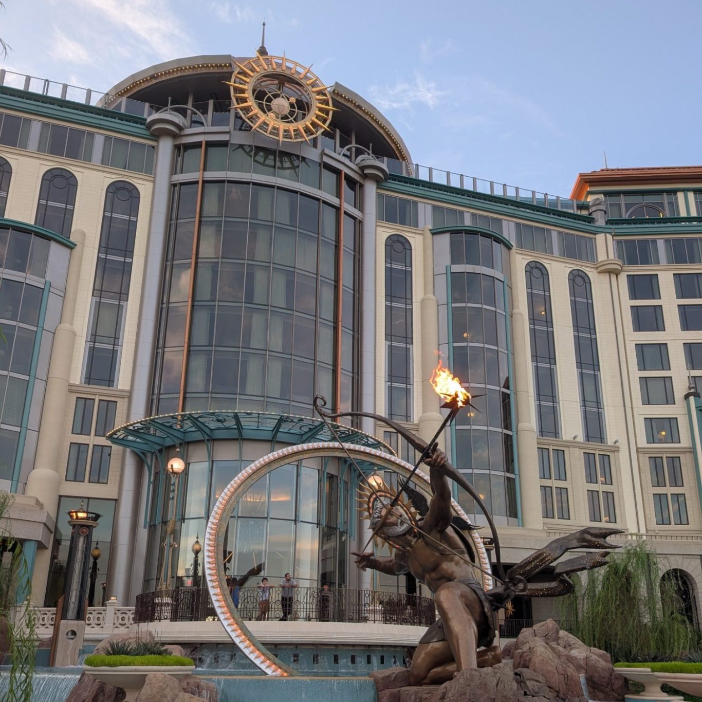 A grand building with a large clock, featuring a statue holding a torch in the foreground.