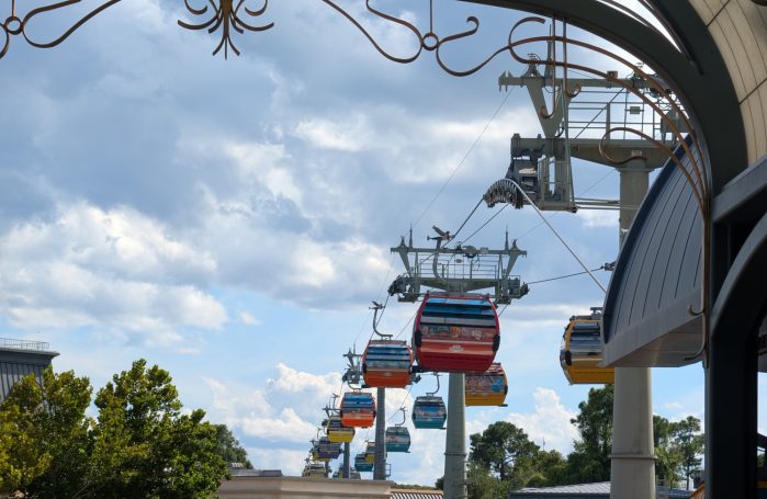 A row of gondolas on the Disney Skyliner system against a cloudy sky.