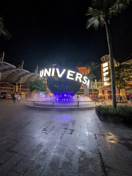 Illuminated Universal Studios globe at night, surrounded by palm trees and water features.