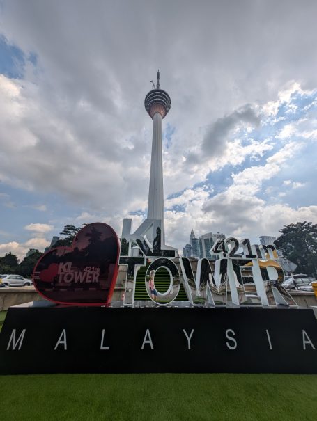 Kuala Lumpur Tower with promotional signage and cloudy sky.