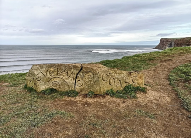 View of the North Sea from the Cleveland Way covered by a cloudy sky, with a rock sign in the forefront of with the words 'Cleveland Coast'