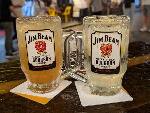 Two glasses of Jim Beam bourbon with mixers, resting on coasters at a bar in Chinatown in Singapore.