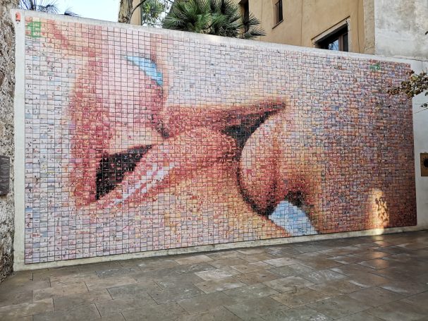 Mural of coloured tiles making up lips kissing, known as The World Comes To Life With Each Kiss in Barcelona