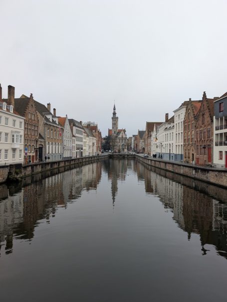 Canal lined with historic buildings, reflecting on still water under a grey sky.