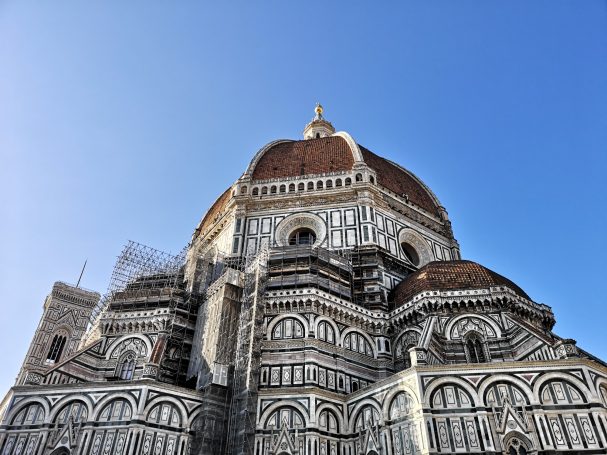 The dome of Cathedral of Santa Maria del Fiore under a clear blue sky, partially covered with scaffolding.
