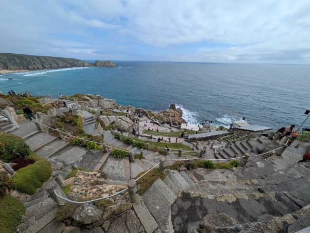 The Minack Theatre on a cliffside with ocean views and stone seating steps.