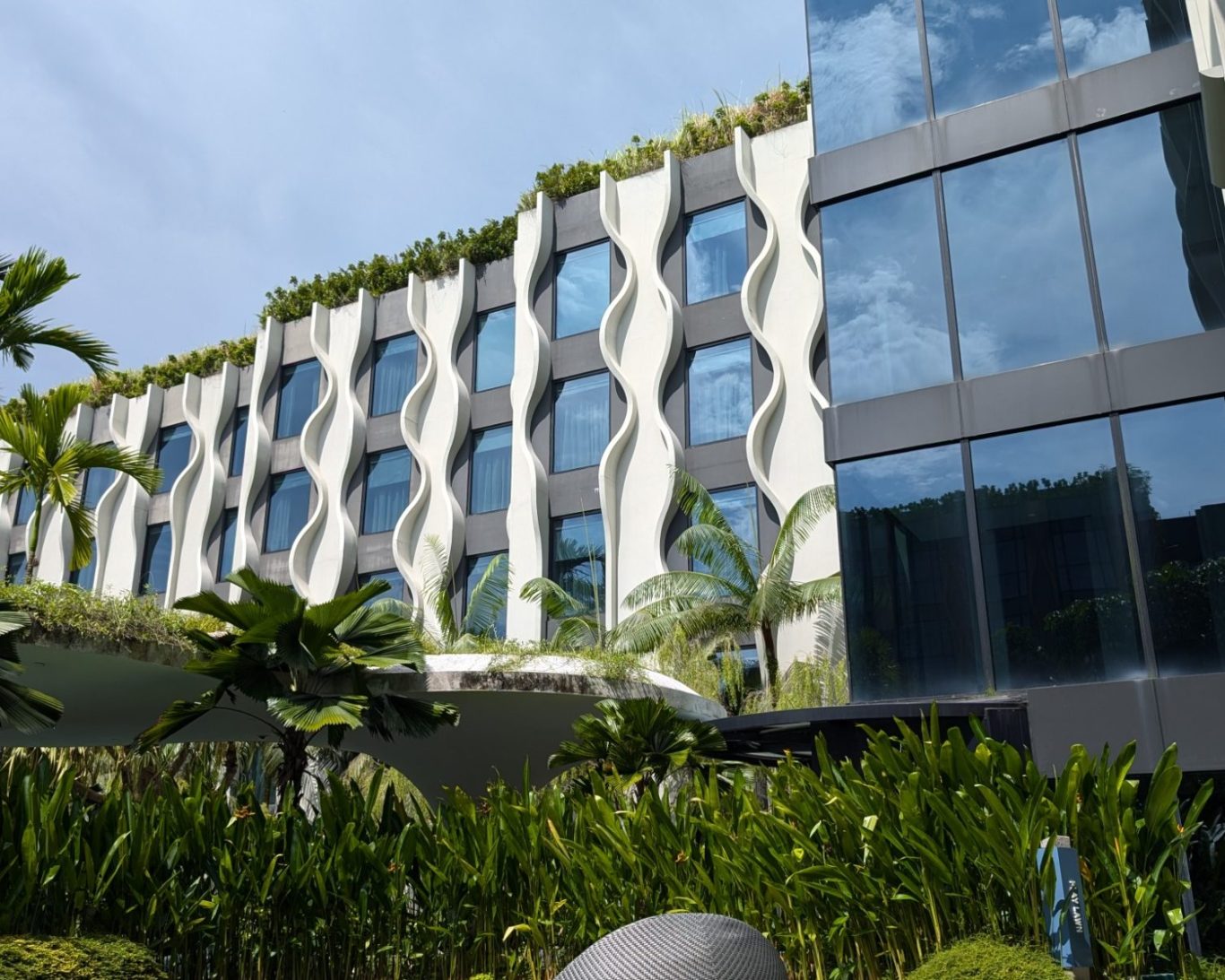 Modern building with unique wave-patterned façade and lush greenery.