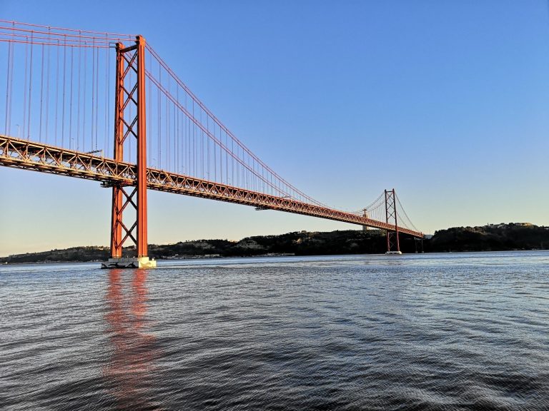 Red Ponte 25 de Abril bridge spanning a river, against a clear blue sky in Lisbon