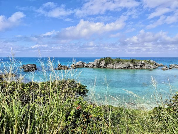 Scenic coastal view with turquoise waters, rocky islands, and lush greenery under a blue sky.
