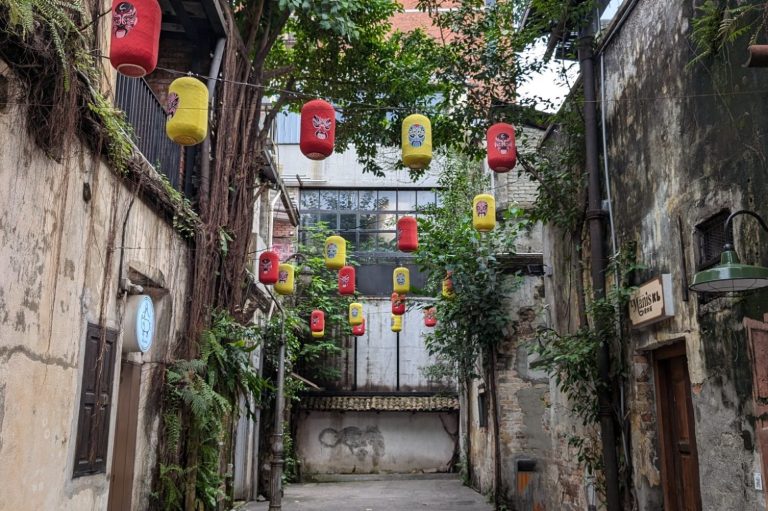 The narrow street of Kwai Chai Hong, home to colourful lanterns hanging above with overgrown greenery and old buildings in Kuala Lumpur.