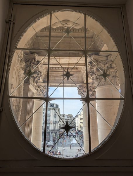 View through an oval window showcasing columns and a city street beyond.