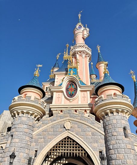 Fairy-tale castle with pink turrets and blue spires against a clear blue sky.