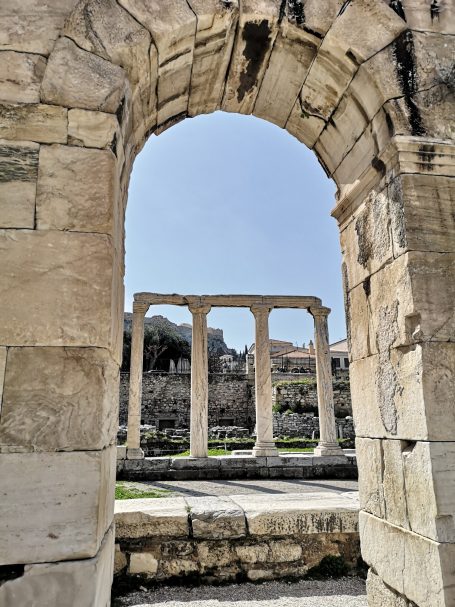 View through an archway of ancient ruins with stone columns and blue sky, located at Hadrian's Library in Athens.