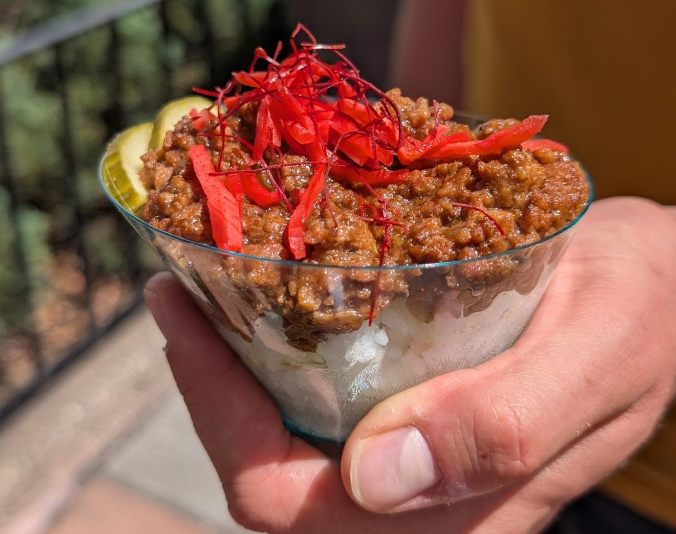 A person holding a bowl of chili topped with red garnishes and lime slices.