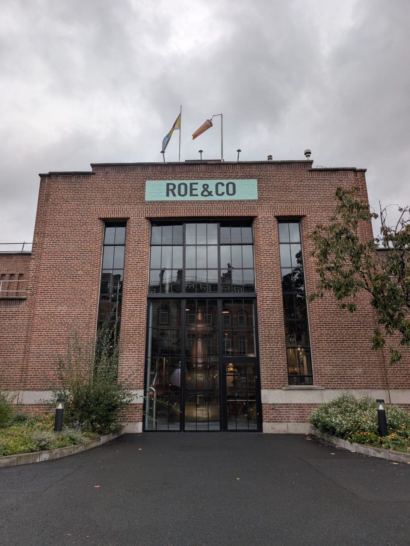 Brick building entrance with large glass doors, "ROE & CO" sign above, and flags on the roof.