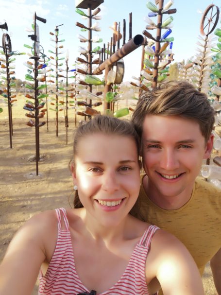 I&B's Founder & Husband posing with colourful glass bottles arranged on poles, to look like trees at Elmer’s Bottle Tree Ranch.