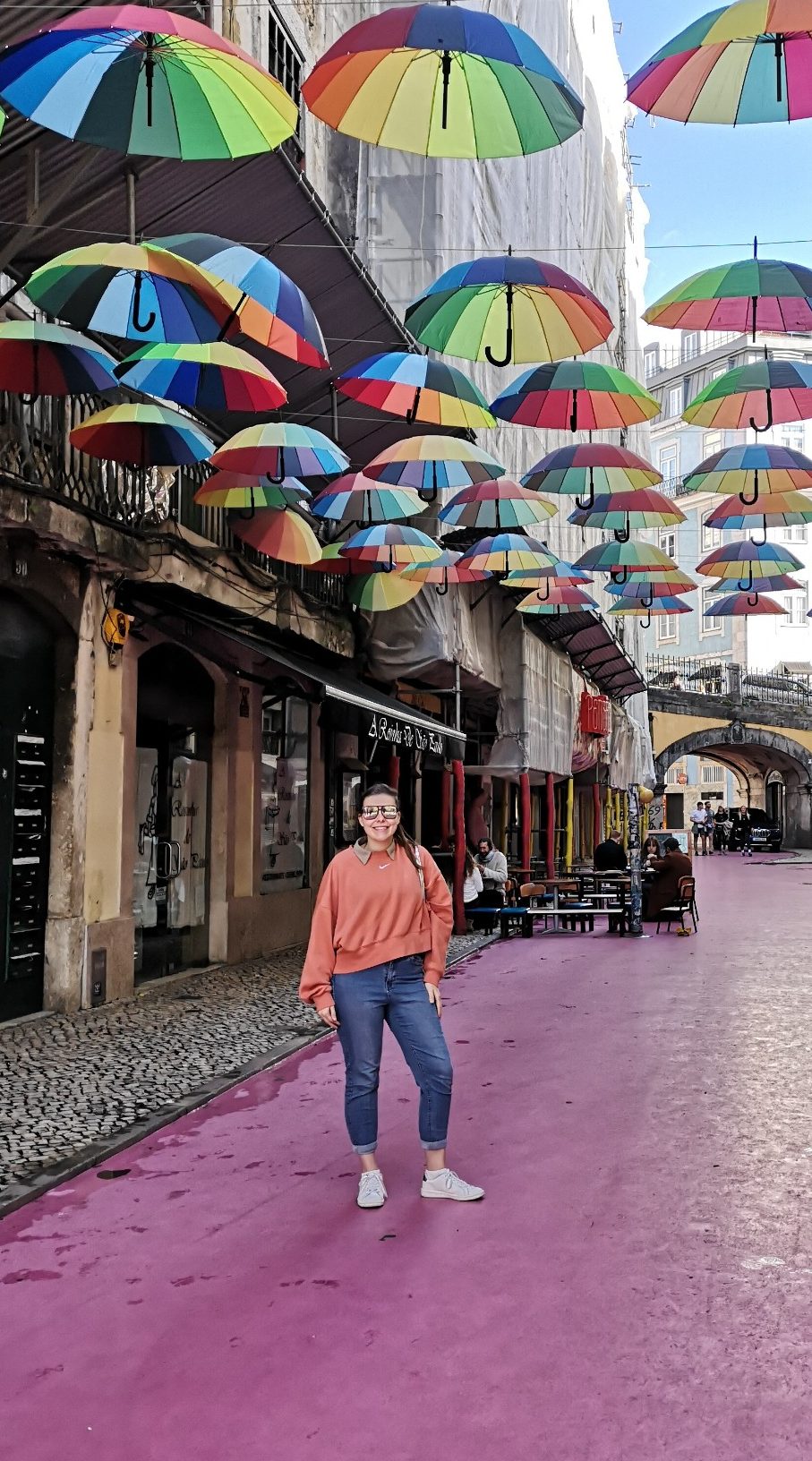 I&B's Founder posing on 'Pink Street' in Lisbon. Colourful umbrellas cover the street above and the floor is painted pink.