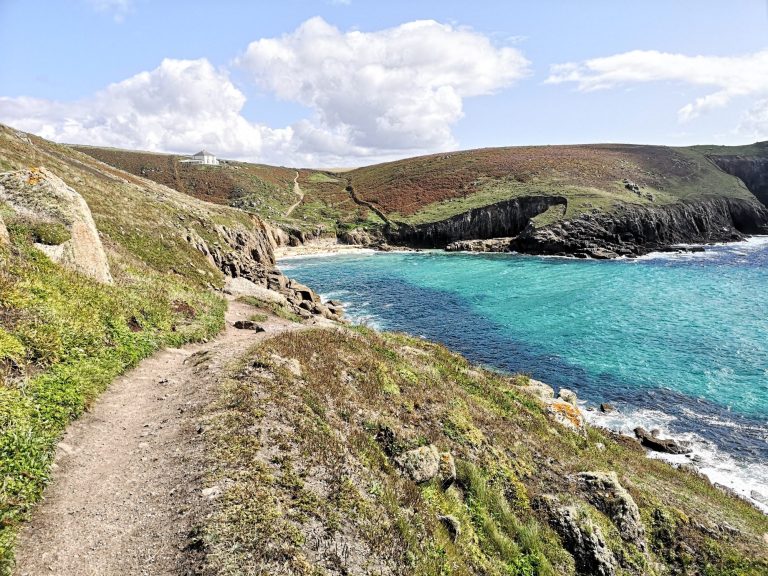 Coastal path leading to a sandy beach with turquoise waters and green hills.