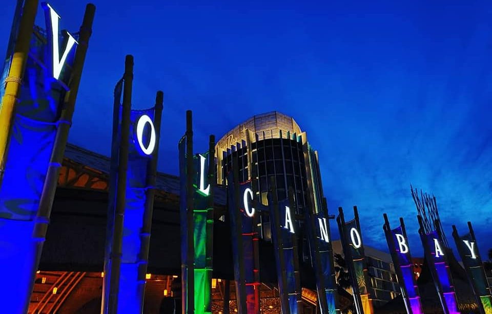 Vibrant illuminated signs of Volcano Bay against a twilight sky.