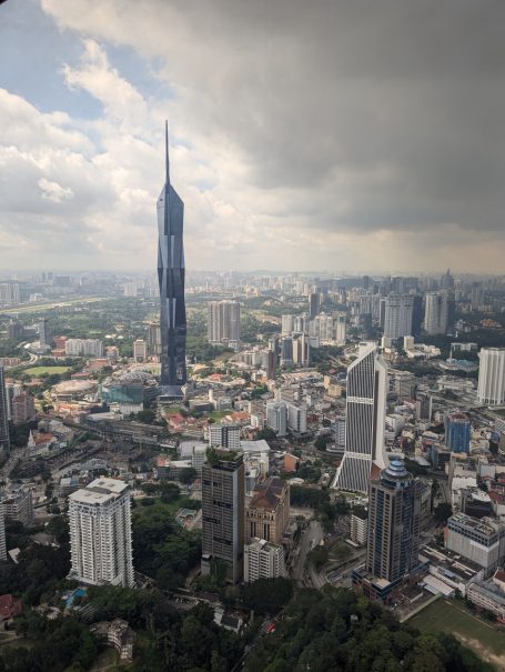 View of a city skyline featuring a tall tower amidst urban buildings and cloudy skies.