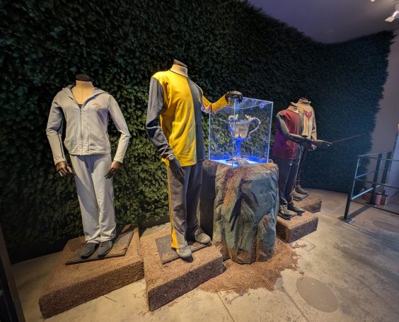 Display of mannequins dressed in sports outfits, alongside a lit glass showcase. Located at the Harry Potter Studio Tour, London.