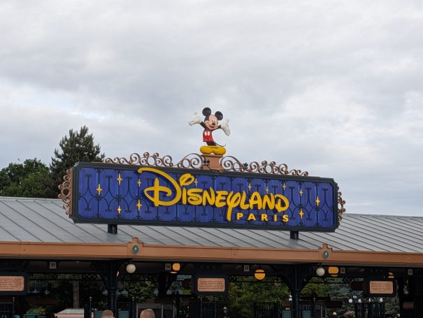 Sign for Disneyland Paris with Mickey Mouse atop a vibrant blue logo.