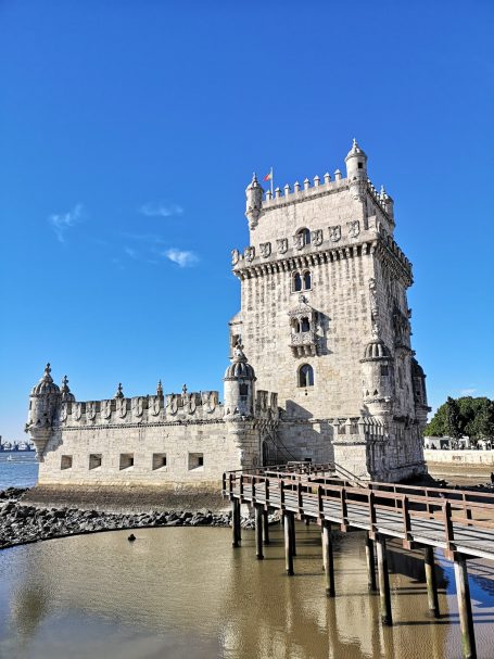 Belem Tower standing by the river, with a clear blue sky in the background.