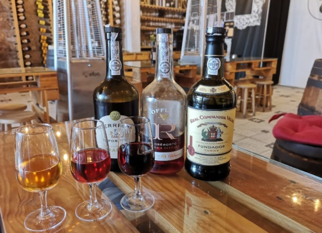Four glasses of different coloured spirits in front of three bottles on wooden table at Quinta do Noval - Gaia in Porto.
