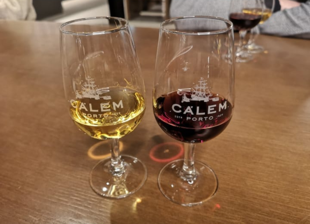 Two wine glasses on a wooden table, one with white port wine and the other with red port wine, the tastings at Calem Caves Winery in Porto.
