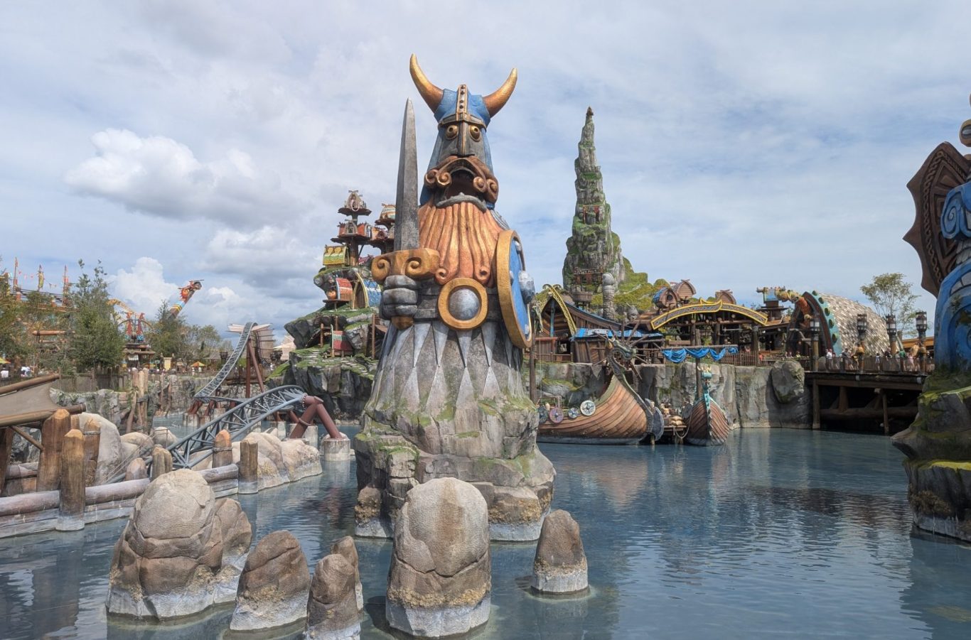 Theme park landscape featuring structures with Viking motifs by a water body under a cloudy sky.