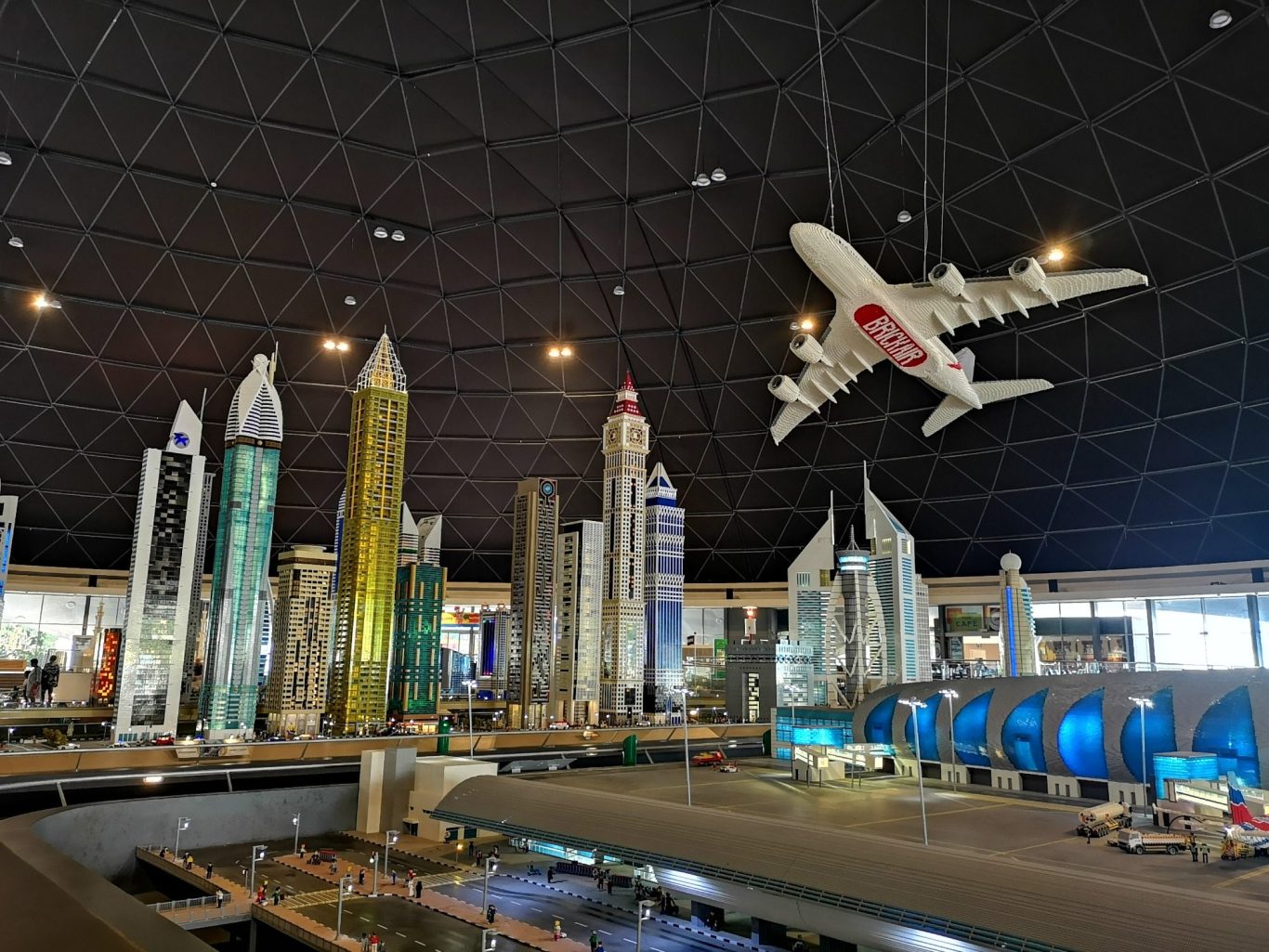 Model city skyline with tall buildings and a hanging airplane in a darkened space.