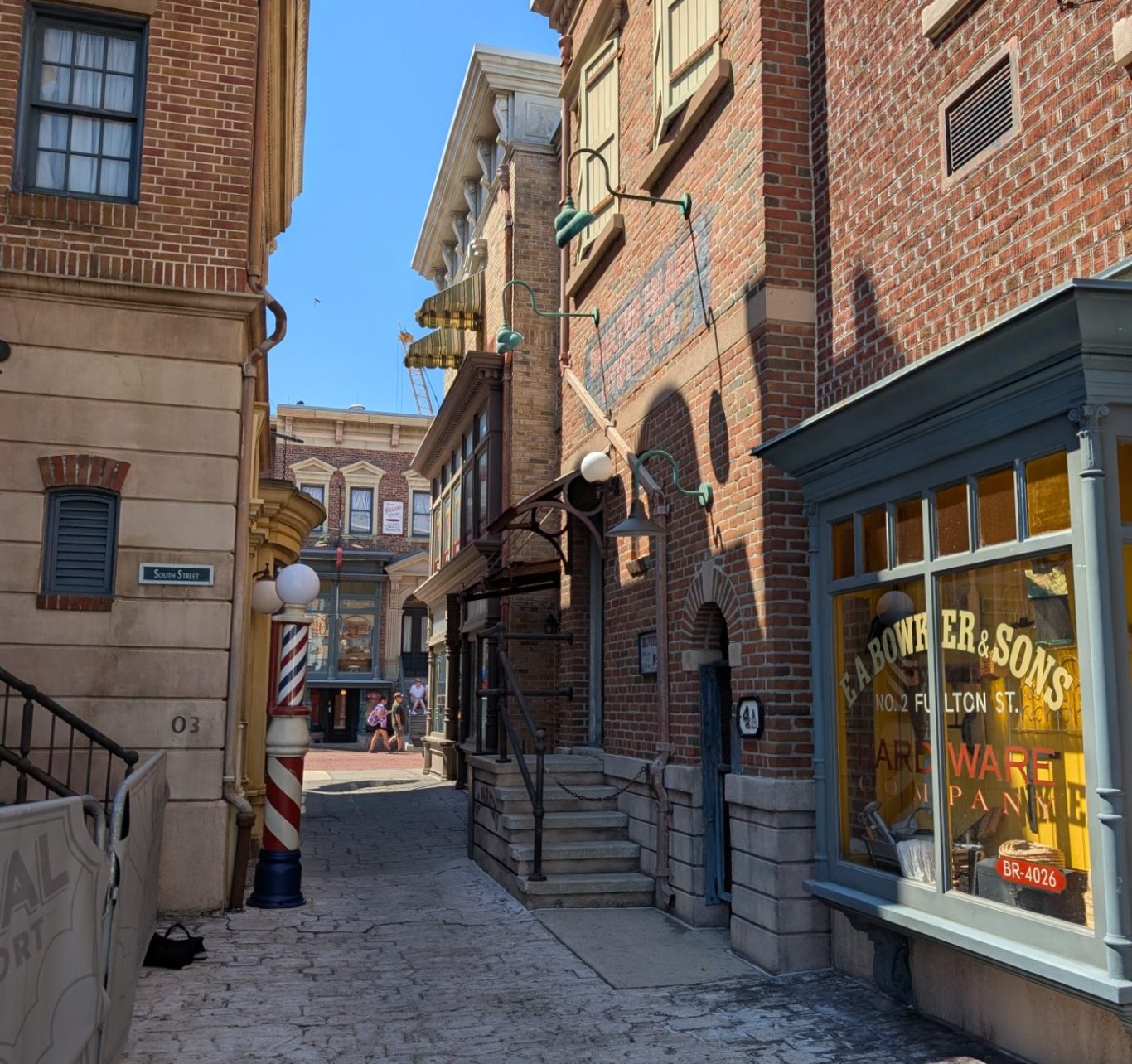 Narrow alleyway with brick buildings and a shop window, sunny blue sky above.