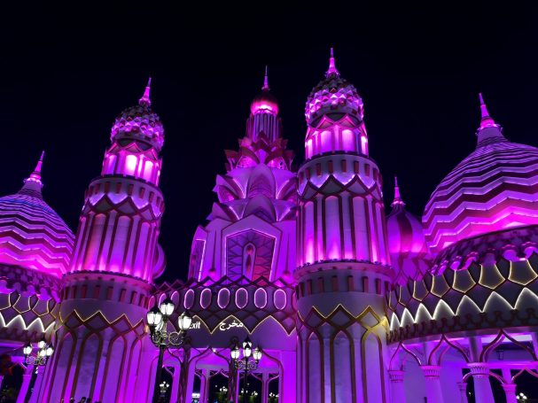 A brightly illuminated architectural structure with pink and purple lights at night, located at Global Village in Dubai.