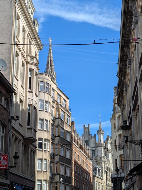 Narrow street in Brussels with historic buildings and spires under a blue sky.