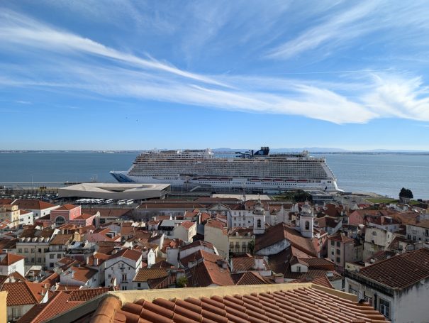 View of coastal city with rooftops, leading to a large cruise ship in the distance.