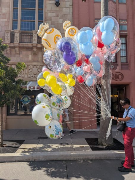 A person holds a cluster of colourful balloons outside a building.