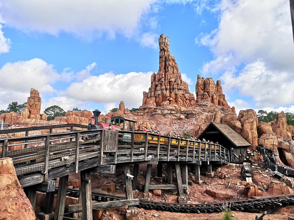 Rocky landscape with a wooden bridge leading to a themed attraction under a cloudy sky.