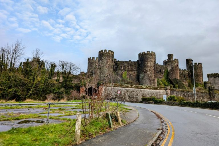 Medieval Conwy castle with towers, surrounded by greenery and a winding road.